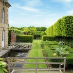 garden architecture a long garden with hedgerows opposite a stone building UXRSKPU