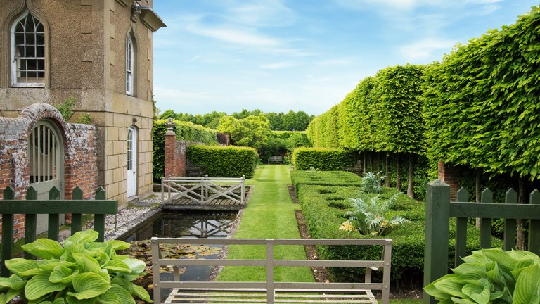 garden architecture a long garden with hedgerows opposite a stone building UXRSKPU