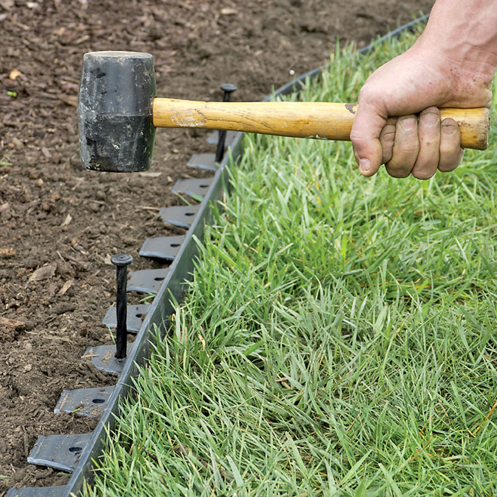 garden edging man using rubber mallet to install edging around garden bed and grass TGWTBIH