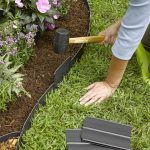 lawn edging woman kneeling outside her garden bed in the grass while pounding in PLHESUM