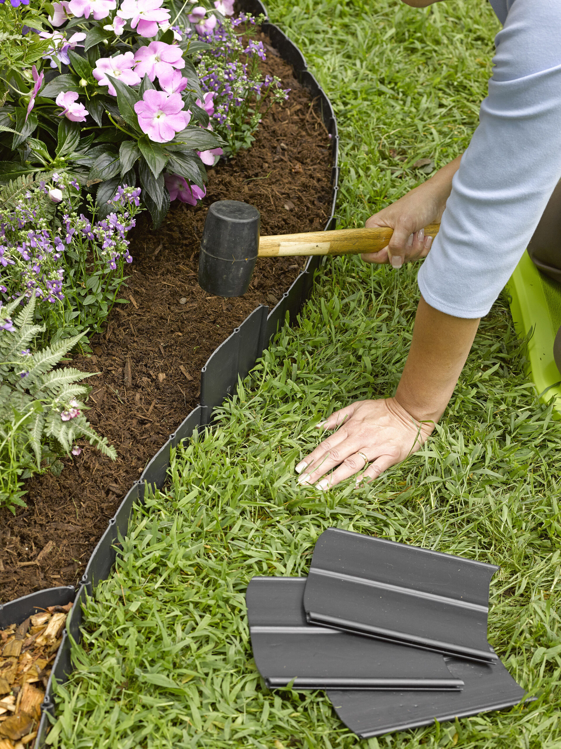 lawn edging woman kneeling outside her garden bed in the grass while pounding in PLHESUM